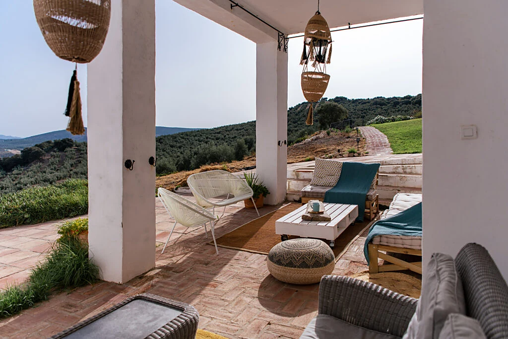 Shaded terrace lounge with woven lamps, armchairs and hillside views