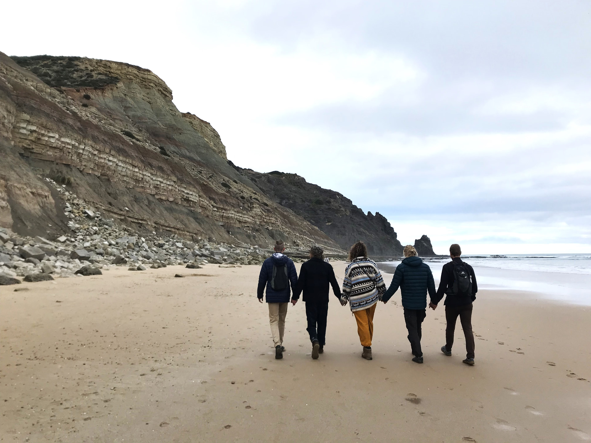 The group walking hand in hand along a beach below the cliffs (impression)
