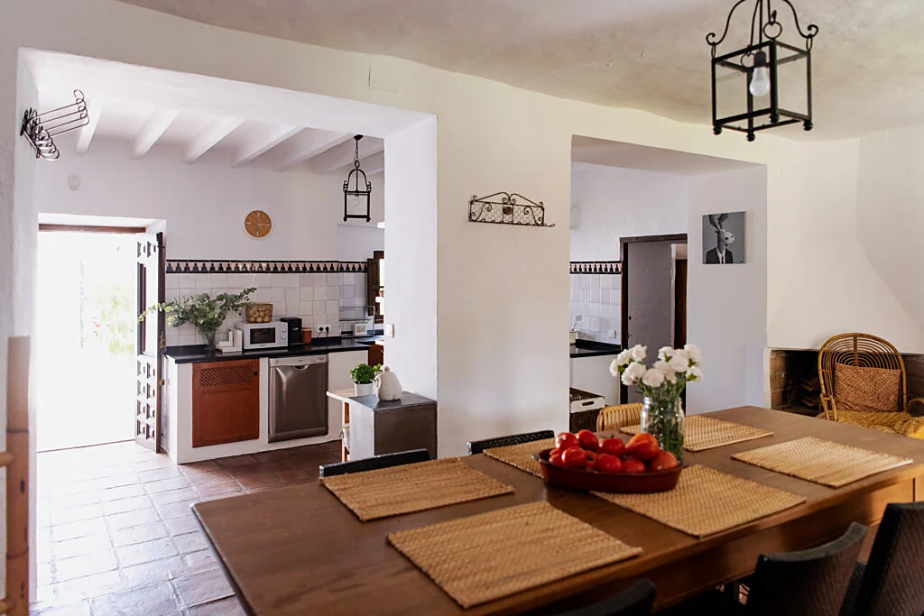 Long dining table set with woven placemats, opening onto the sunlit kitchen