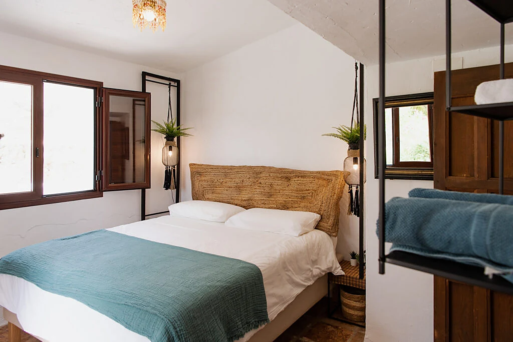 Bright double bedroom with a teal throw and hanging plant lamps