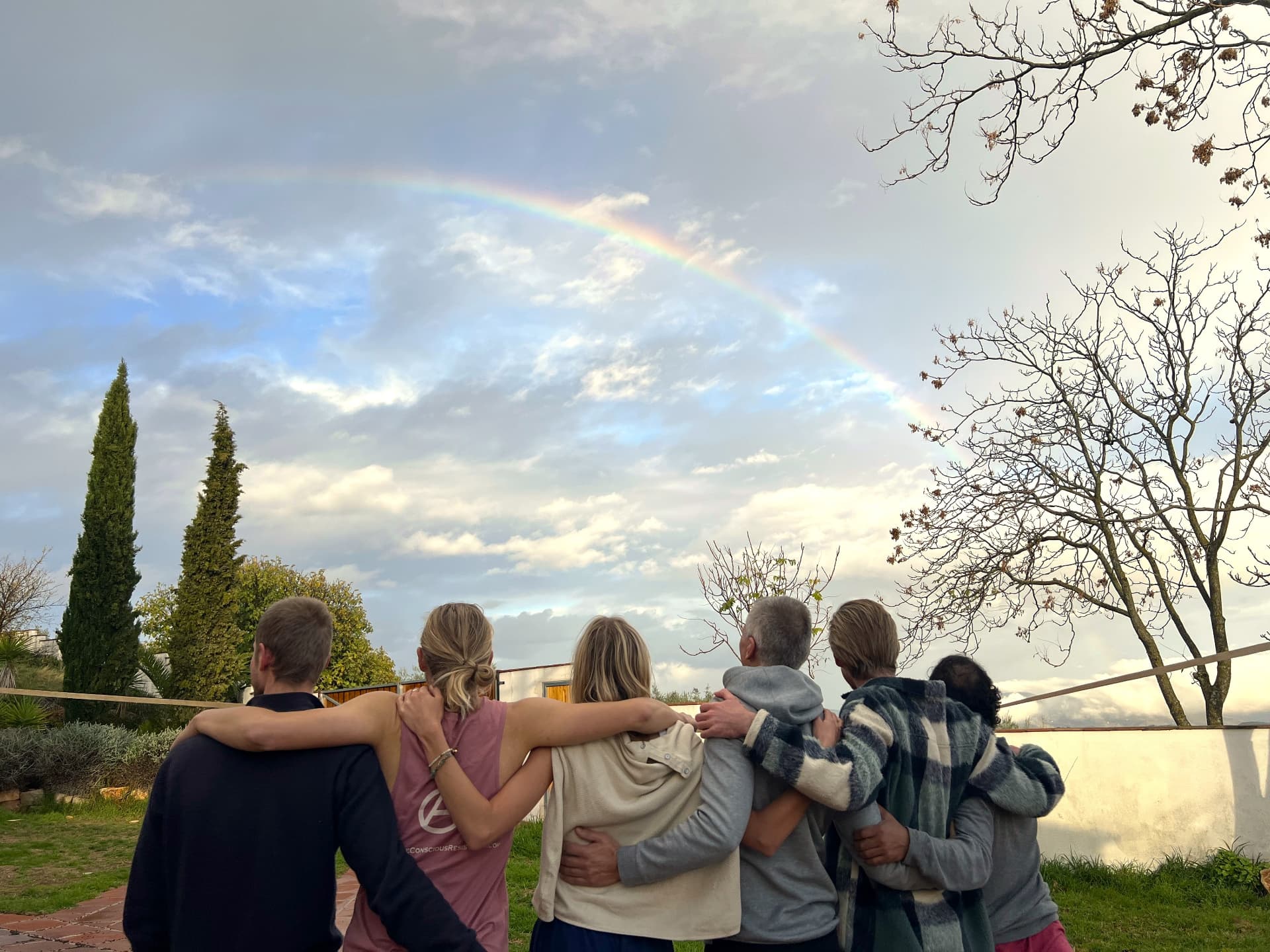 A group standing arm in arm beneath a rainbow